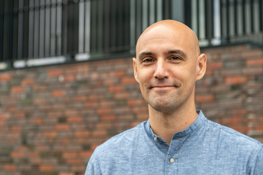 The portrait photo shows Thorben Cordes in a light blue shirt. A brick wall and a black railing can be seen blurred in the background.