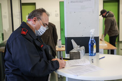 Ein Feuerwehrmann steht an einem Stehtisch und füllt Unterlagen aus.