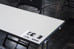 Ein weißer Tisch, auf dem ein Zettel mit der Aufschrift "Block E, Platz 37" liegt.