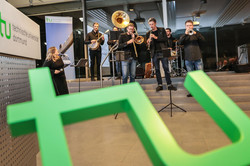 Eine Band mit Blasinstrumente, im Vordergrund das grüne TU-Logo