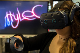 Frau mit VR-Brille steht vor einem Bildschirm, auf dem Hylec steht. 