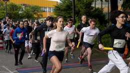 Mehrere Personen in Sportoutfit halten einen Staffelstab und laufen.