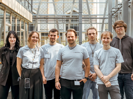 Foto: Eine Gruppe von Menschen steht nebeneinander in einer hellen Halle mit Glasdach.