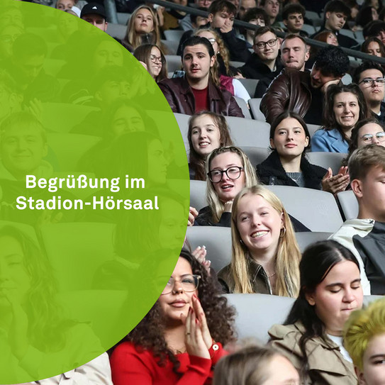Eine Gruppe von jungen Menschen sitzt auf der Tribüne eines Stadions. Links im Bild befindet sich ein grüner Halbkreis mit der Aufschrift "Begrüßung im Stadion-Hörsaal".