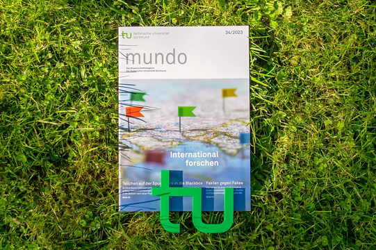 mundo_international forschen Die Ausgabe 34/2023 der Forschungszeitschrift mundo liegt im Gras, am unteren Rand liegt ein kleines, grünes TU-Logo auf der Zeitschrift.