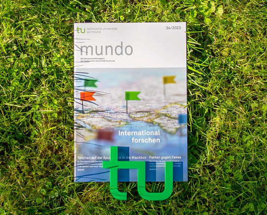 Die Ausgabe 34/2023 der Forschungszeitschrift mundo liegt im Gras, am unteren Rand liegt ein kleines, grünes TU-Logo auf der Zeitschrift.
