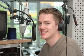 Ein Student sitzt mit Kopfhörern und Mikrofon in einem Tonstudio.