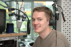 A student sits in a recording studio with headphones and a microphone.