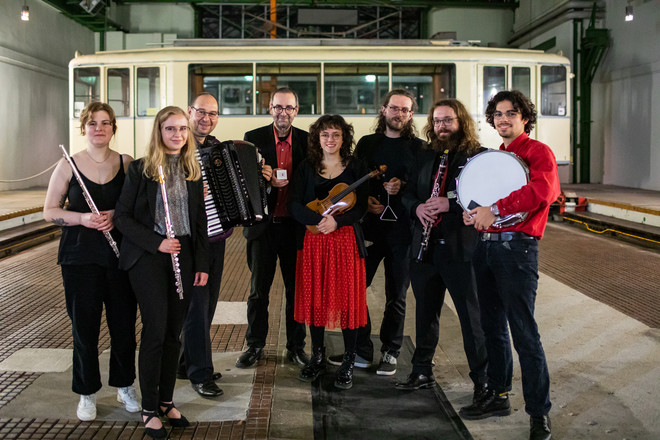 Acht Musiker*innen des Ensembles für Neue Kammermusik stehen nebeneinander mit Instrumenten in den Händen.