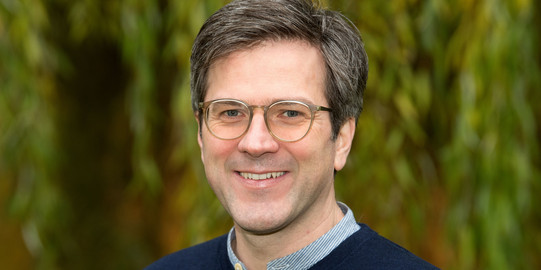 Portrait photo of Bernd Sommer, in the background blurred a weeping willow. 