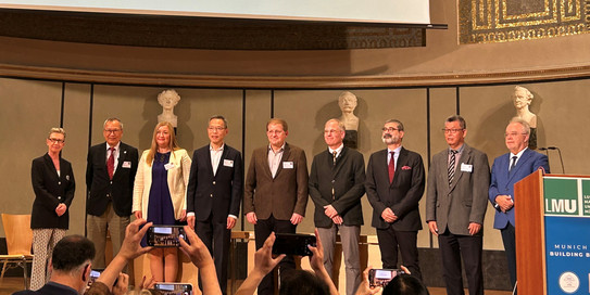 Gruppenbild von sieben Personen auf einer Bühne, alle sind sehr formell gekleidet.