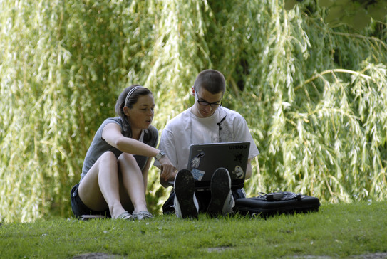 Zwei Studierende sitzen auf der Wiese und schauen sich etwas auf einem Laptop an.