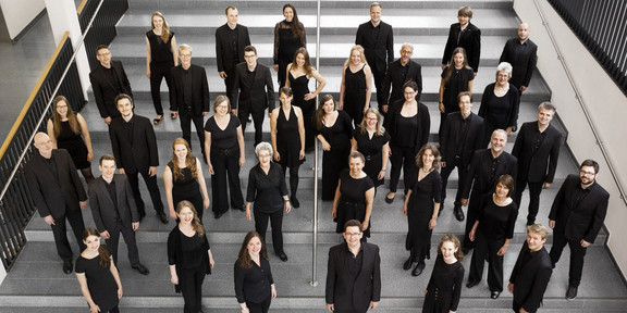Ein Gruppenfoto vom Kammerchor der TU Dortmund. Die schwarz gekleideten Musiker*innen sind von oben fotografiert.