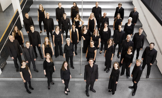 Der Kammerchor der TU Dortmund Ein Gruppenfoto vom Kammerchor der TU Dortmund. Die schwarz gekleideten Musiker*innen sind von oben fotografiert.