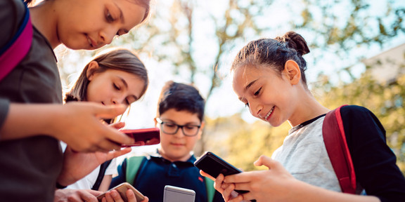 Foto: Eine Gruppe Schüler*innen steht im Kreis und hält Smartphones in den Händen.