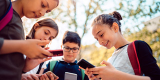 Foto: Eine Gruppe Schüler*innen steht im Kreis und hält Smartphones in den Händen.