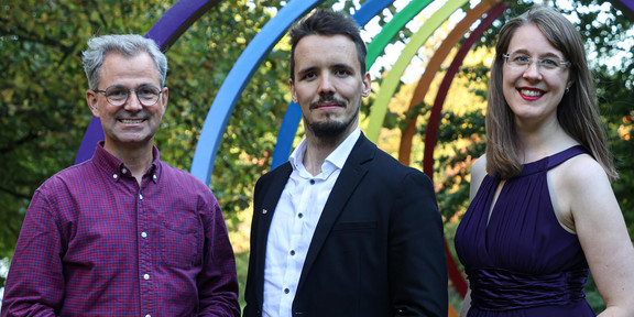 Drei Personen stehen vor der Skulptur "Spektral-Ringe" auf dem Campus der TU Dortmund