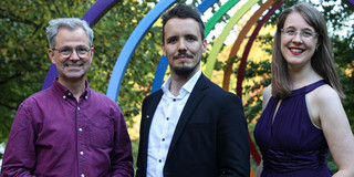 Drei Personen stehen vor der Skulptur "Spektral-Ringe" auf dem Campus der TU Dortmund