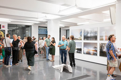 Auf dem Bild sind verschiedene Menschen sowie gemalte Bilder in einem Ausstellungsraum zu sehen.