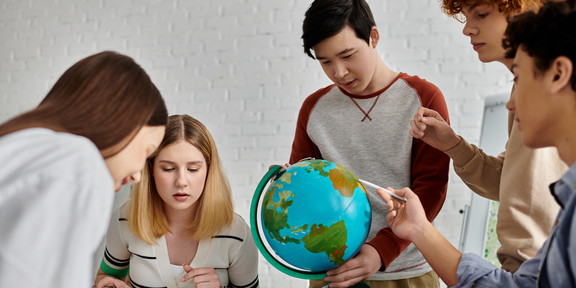 Foto: Mehrere Personen betrachten gemeinsam eine Karte und einen Globus auf einem Tisch.