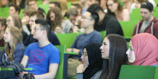 Many students in a lecture hall with green benches.