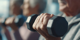 Auf dem Foto sieht man eine ältere Person, die eine Hantel in der Hand hält und das Gewicht stemmt.