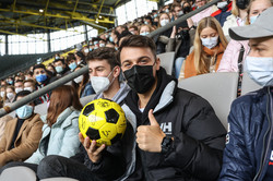 Nahaufnahme von einem Erstsemesterstudierenden, der auf einer überdachten Tribüne in einem Fußballstadion sitzt und einen Fußball in der Hand hält.