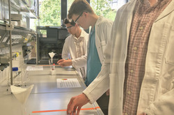 Veranstaltung "DNA - Was Erdbeeren und wir gemeinsam haben" Ein Teilnehmer mit einem weißen Kittel und einer Schutzbrille führt ein Experiment durch.