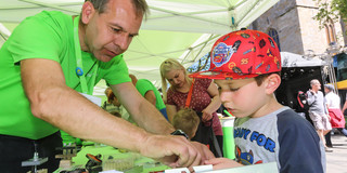Ein in grün gekleideter Mann zeigt einem Jungen ein Experiment