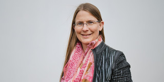Ein Foto einer Frau mit Brille, gemustertem Oberteil und rosa Schal.