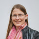Ein Foto einer Frau mit Brille, gemustertem Oberteil und rosa Schal.