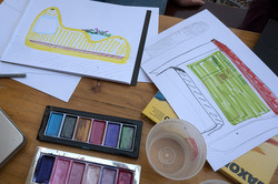 Photo: Drawings, brushes, and watercolor paints lie on a table.