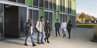 Internationale Studierende Internationale Studierende laufen auf dem Gehweg vor einem Campusgebäude.