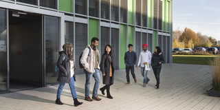 Internationale Studierende laufen auf dem Gehweg vor einem Campusgebäude.