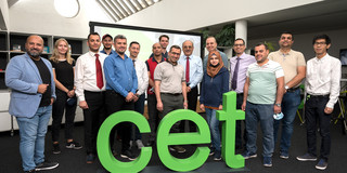 Mehrere Personen stehen in einer Reise und vor ihnen ist das grüne Logo des CET platziert.