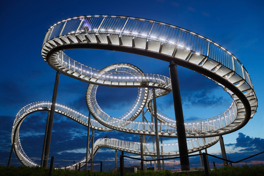 Beleuchtete Treppenskulptur "Tiger and Turtle", ähnlich wie eine Achterbahn gestaltet, vor abendlichem Himmel