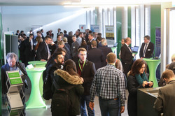 Several people are standing in a foyer, information stands are set up on the edge