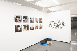 Eine Installation der Ausstellung zeigt einen Schlafsack und eine dünne Matratze auf dem Boden. Darüber hängen Portraitfotos verschiedener Obdachloser.