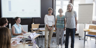 Gruppenfoto von drei Personen, links sitzen Konferenzteilnehmer