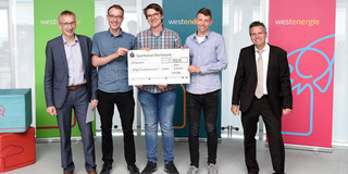Das Siegerteam des Westenergie Manager Cups Gruppenfoto von fünf Männern im Business-Outfit vor drei Werbebannern. Links steht Prof. Andreas Hoffjan, in der Mitte stehen drei Studenten und halten einen großen Sparkassen-Check, rechts steht Achim Schröder.