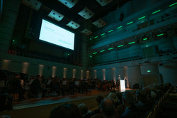 View of the darkened stage with lectern, orchestra and screen