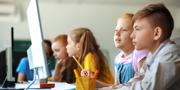 Das Bild zeigt Kinder von der Seite, die an Computern sitzen.