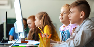 Das Bild zeigt Kinder von der Seite, die an Computern sitzen.