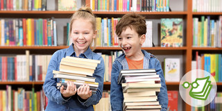 Ein Junge und ein Mädchen stehen vor einem großen Bücherregal und halten jeweils einen Stapel Bücher in den Händen. 