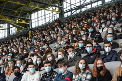 Welcoming of the first-semester students First-year students sit in covered bleachers at a soccer stadium. They are wearing mouth-to-nose coverings.