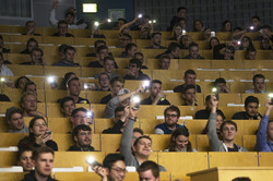 Ein Publikum im Hörsaal leuchtet mit den Taschenlampen am Handy.