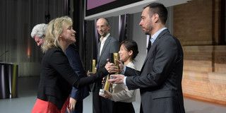 Eine Frau überreicht einem Mann einen schwarz-goldene Trophäe auf einer Bühne.