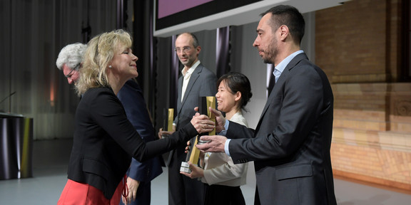 Eine Frau überreicht einem Mann einen schwarz-goldene Trophäe auf einer Bühne.