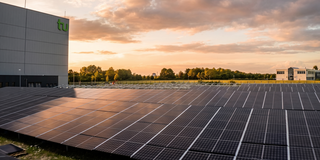 Photo: A large field of solar panels lies next to a building.