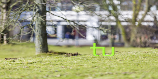 TU Logo auf einer Wiese neben einem Baum